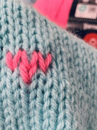 Close-up of pink heart embroidery stitched onto aqua knitted fabric, handmade heart detail by Happy Sheep Creations
