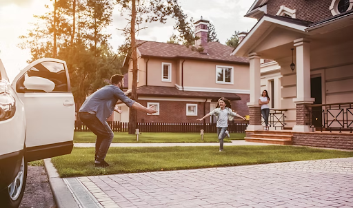 Man welcomes a young girl running toward him across the front lawn of a suburban home.