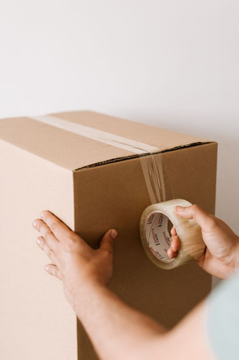 Hands sealing a large cardboard moving box with clear packing tape.