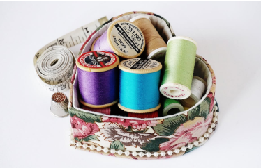 Heart-shaped floral sewing box with colorful spools of thread, measuring tape, and thimble – sewing supplies for DIY crafts and tailoring.