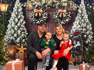 Four people sitting in front of a holiday display, the two parents are holding the children on their lap and everyone is smiling at the camera.
