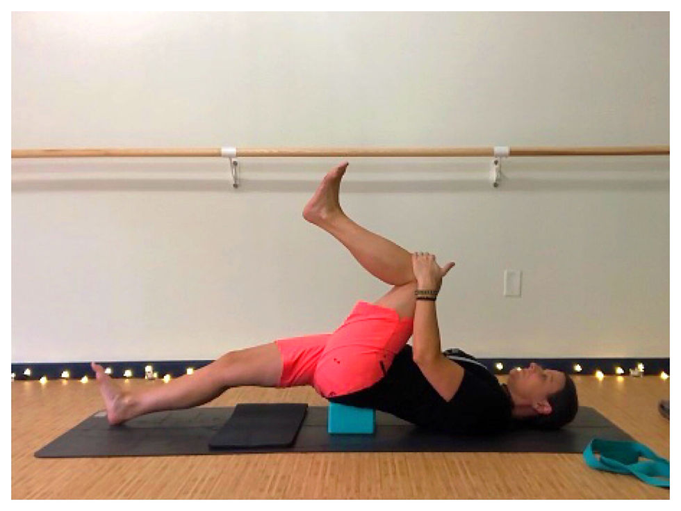 Reclined Knee to Chest position for a person with limited knee flexion, using a yoga block supporting the pelvis to lengthen the hip flexors.
