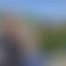 A man and a woman standing by a fence in a playground in Bergen. Hills behind them, the sun is shining, they are wearing sunglasses and smiling.
