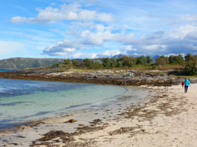 Sandy beach on Sommaroy Island, crystal clear torquoise waters. Mother and autistic child walking together in the distance