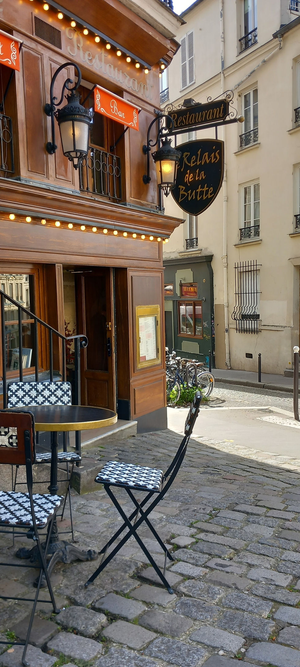 Cobbled street corner in Montmartre, Paris. Distinctive Parisienne bistro chairs with black and white diamond patter surround a small round table in front of Relais de la Butte, a popular restaurant in Montmartre Paris.