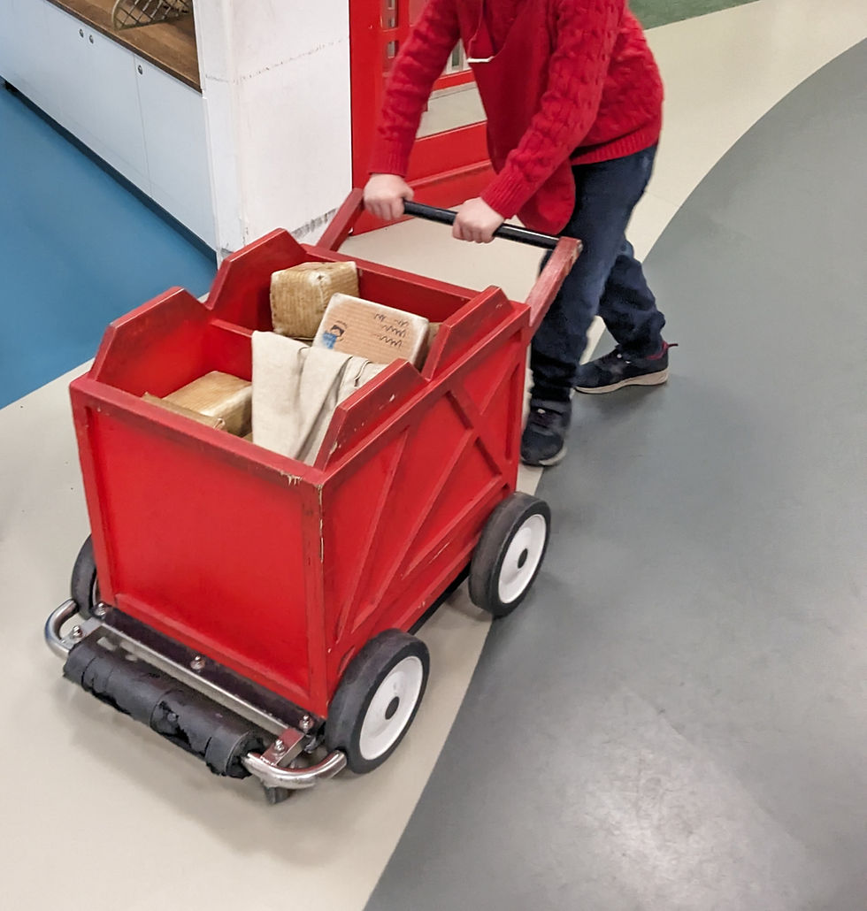 Autistic child enjoying role playing as a postie delivering and collecting post with a trolley at SORTED! play space, The postal Museum, London