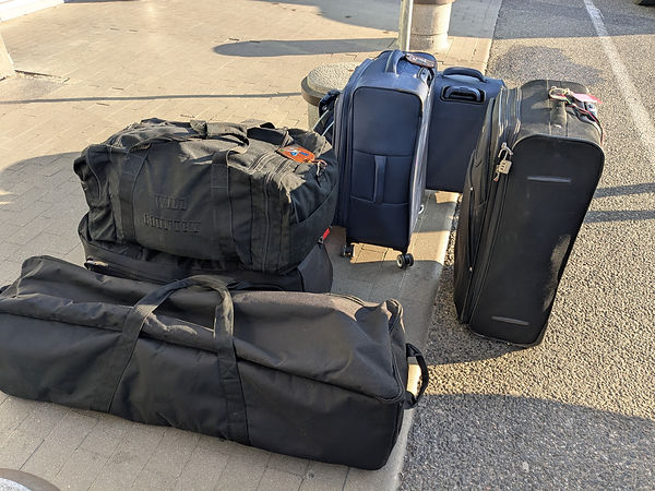 Suitcases on airport forecourt, a mix of soft bags and harder shell cases.