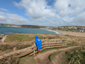 Autistic child standing on fence railing high up on Burgh Island, looking at the cliffs and sandy beaches of Bigbury in the distance.