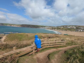 Autistic child standing on fence railing high up on Burgh Island, looking at the cliffs and sandy beaches of Bigbury in the distance.
