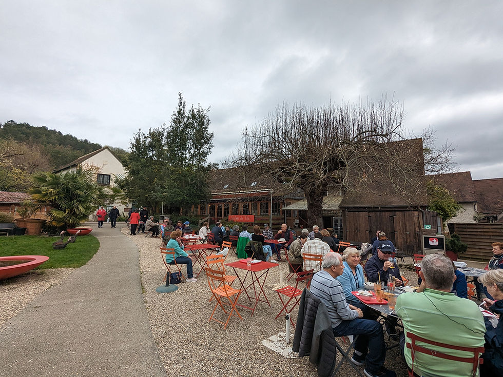 La Capucine restaurant outdoor seating area in Giverny village featuring a spacious gravel patio with orange tables and chairs near a grassy pond for sensory-friendly family dining.