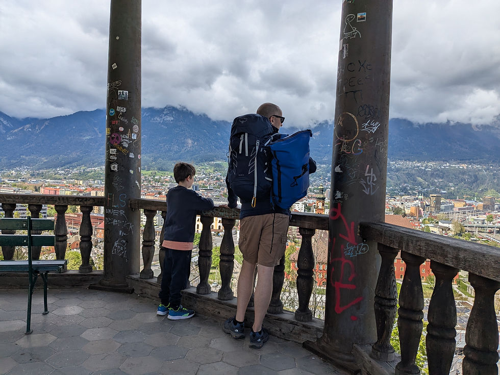 Father and autistic child standing in a large stone rotunda with waist high balustrade. They are admiring the view of houses and cloud topped mountains in the valley of Innsbruck far below.