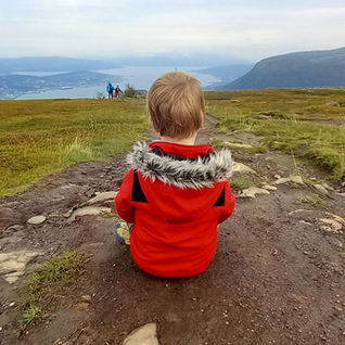 An autistic boy sitting on a rock on Mt Floya, at the top of the Fjellheisen Cable Car in Tromso. View of hills and river.