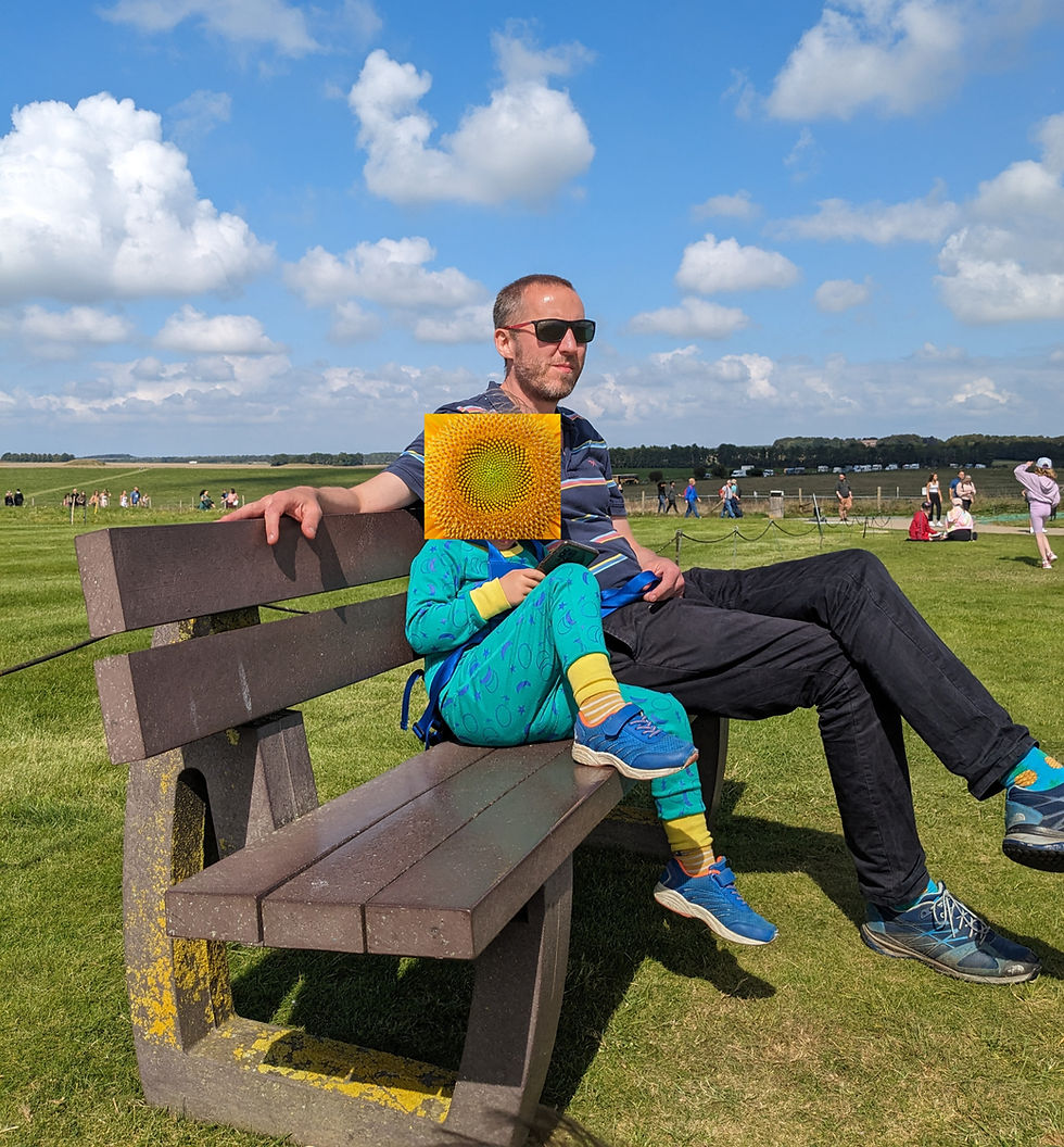 A man and an autistic boy sitting on a bench enjoying some decompression time while looking at the Stonehenge stone circle.