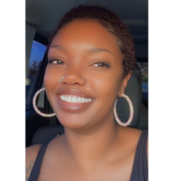 Smiling woman, curly hair, hoop earrings, nose ring, bright smile.