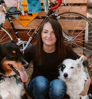 Woman with black and white dogs, bike, and BEAR CROSSING sign.