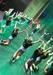 Performers form a circle on stage with on their knees with arms outstretched.