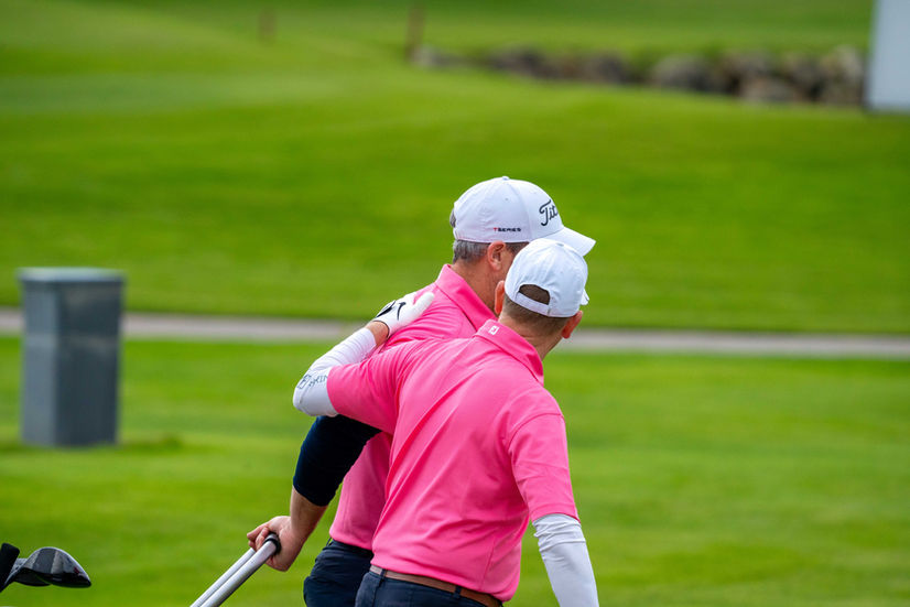 Two golfers in pink shirts walk the course