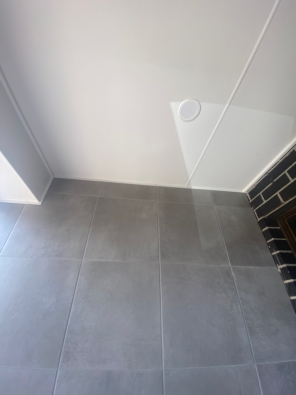 Gray tiled floor with a white wall featuring a circular vent. Partial view of a window on the right side, modern and minimalistic.