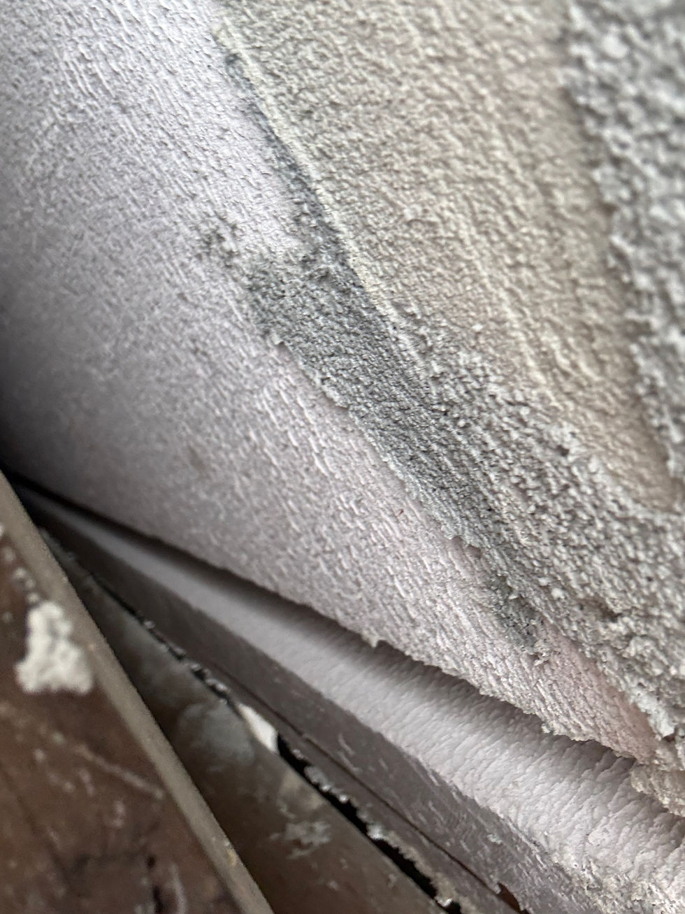 Close-up of rough-textured white and gray walls meeting at an angle, with some chipped paint and cracks, creating an aged appearance.