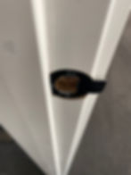 Close-up of a white door edge with a black, damaged latch plate. The background is a gray carpet, giving a worn-out appearance.