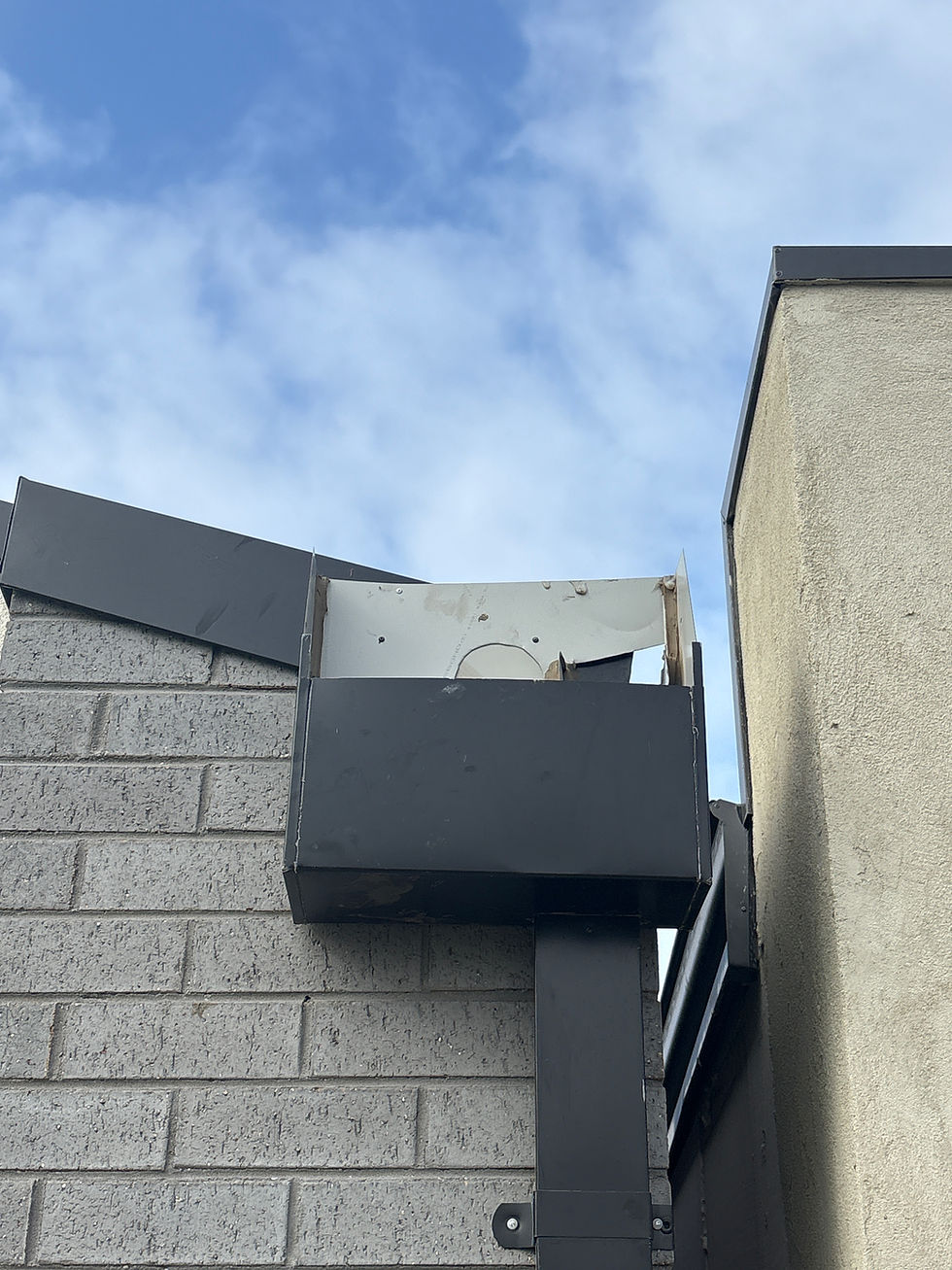 Black drainage pipe on a brick building corner against a blue sky. Some debris is visible in the top section. Mood is calm.