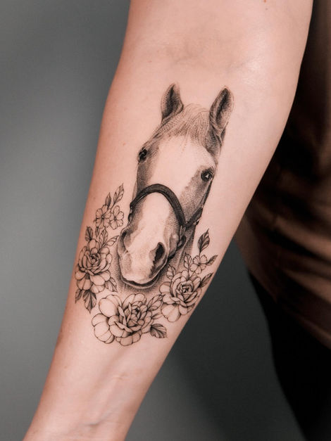 Black-and-grey horse head tattoo surrounded by flowers on the arm.