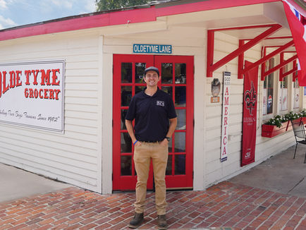 Ross Murphree stands outside Olde Tyme Grocery in Lafayette, Louisiana, in front of the restaurant's historic building and iconic Olde Tyme Grocery sign.