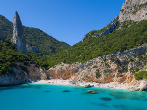 Cala Goloritzé an der Ostküste Sardiniens – idyllische Bucht mit weißem Kiesstrand, türkisblauem Wasser und markanter Felsnadel vor steilen, grünen Berghängen.