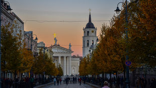 Abendstimmung in der Altstadt von Vilnius mit Blick auf die Kathedrale und den Glockenturm, flankiert von herbstlich gefärbten Bäumen.
