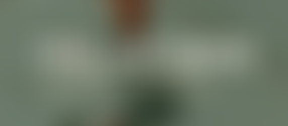 Blog post header image with a dark green-tinted overhead photo of a creative workspace — laptop, orange tumbler, camera, notebook, and pencils on a white wood surface. Bold white text reads "THE ANSWER" with gold text beneath: "TO THE MARKETING PROBLEM YOU'VE BEEN TOO BUSY TO SOLVE."
