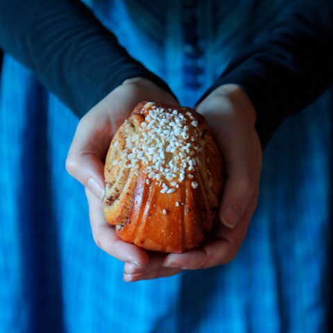 Korvapuusti, jota pitelee kahdella kädellä marttapukuinen nainen