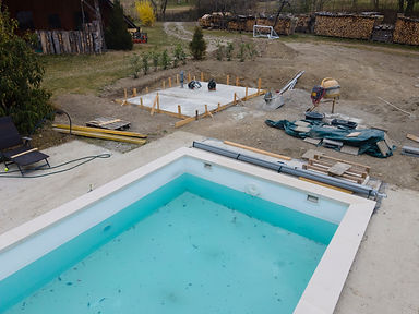 Drone shot of pool construction site with concrete pad for heat pump and pool house in gar