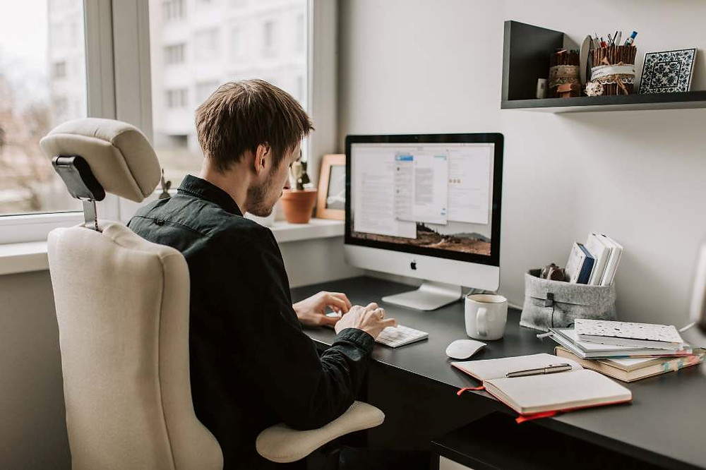 Man sitting in desk chair in front of computer looking at keyboard