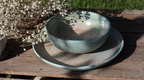 Beautiful bowl and dinner plate featuring light aqua blue variegated glaze. The dinnerware is nestled in small white Baby's Breath flowers.
