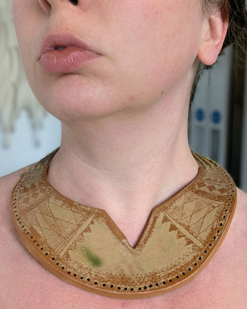 A model wearing a crescent-shaped ceramic pendant made from dark toasted stoneware. The surface features a light yellow-green glaze scratched back to reveal intricate sgraffito patterns.
