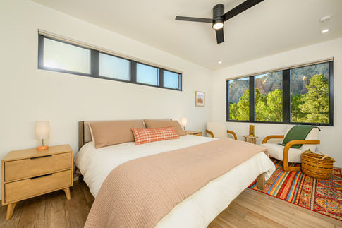 Interior view of a spacious, modern Southwest Contemporary Sedona guest bedroom designed for parents, featuring a large comfortable bed, warm wood accents, and expansive windows offering natural desert views.
