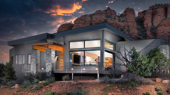 Twilight view of a sustainable custom home in Sedona, featuring a warmly lit entrance and glowing interior spaces as day transitions to night.