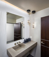 The powder bath for guests features a floating contemporary concrete sink, providing a modern and stylish touch to the space. Concealed wall lighting adds a subtle and sophisticated ambiance, while whimsical pendant lights bring a touch of playfulness to the room. The combination of these elements creates a welcoming and visually appealing environment for guests to enjoy. The design choices reflect a thoughtful consideration for both aesthetics and functionality, ensuring that the powder bath is both practical and visually striking. Overall, the attention to detail in the design of the powder bath contributes to a memorable and enjoyable experience for guests.
