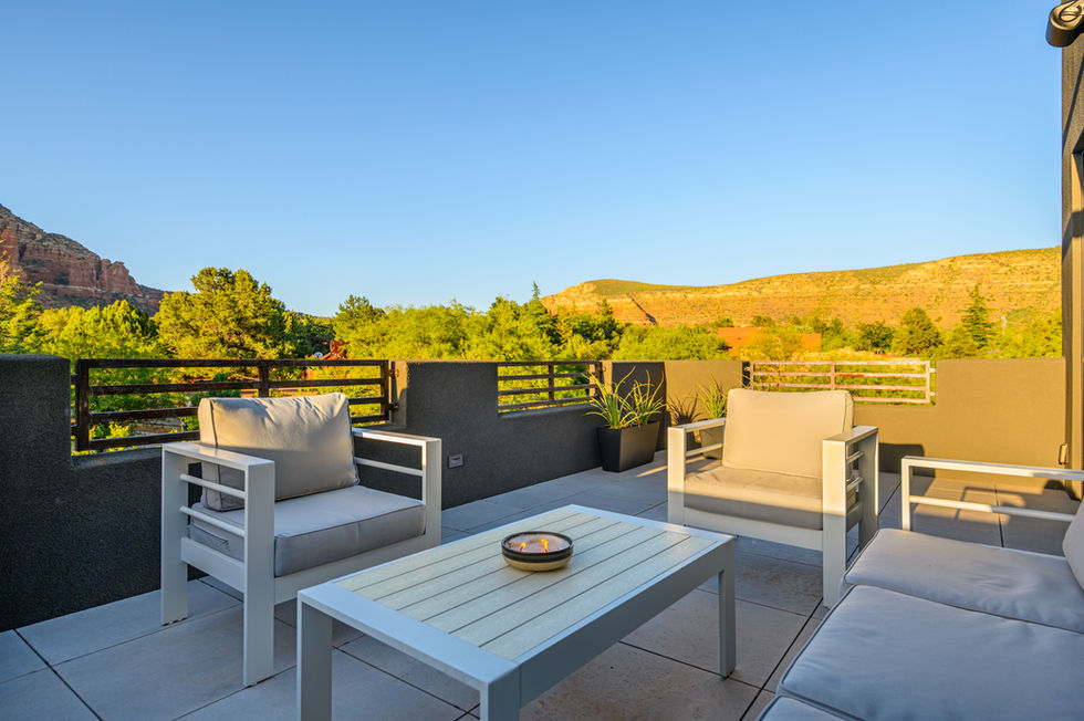 Sunny daytime view of a Southwest Contemporary upper-level deck remodel in Sedona, featuring modern white outdoor lounge furniture and panoramic red rock mountain views.