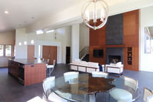 Expansive open-concept great room in a remodeled Sedona home featuring a round glass dining table with white chairs, a living area with white sofas, a large wood-paneled fireplace wall, and bright natural light.