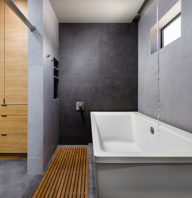 Modern wet room in a luxury custom home featuring a deep white soaking tub, a spacious walk-in shower area, and a unique ceiling-mounted tub filler.