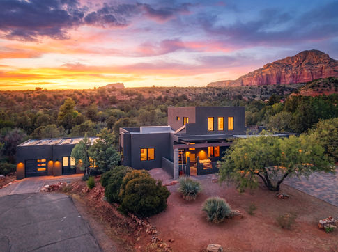 Twilight exterior view of a modern Southwest Contemporary remodel in Sedona featuring glowing warm lights and natural desert landscaping.