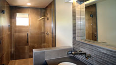 Modern remodeled bathroom featuring a frameless glass shower enclosure, premium textured porcelain ceramic wall tiles, a built-in shower bench, and a contemporary vanity with an integrated sink.