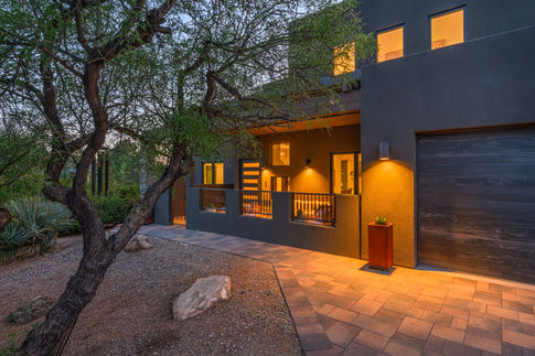 Evening exterior view of a modern Southwest Contemporary Sedona remodel showcasing dark sky compliant exterior downlighting, native trees, and natural boulder landscaping.