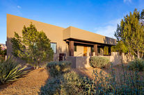 Earth-toned sustainable residential home surrounded by native, drought-tolerant desert landscaping in Sedona under a clear blue sky.