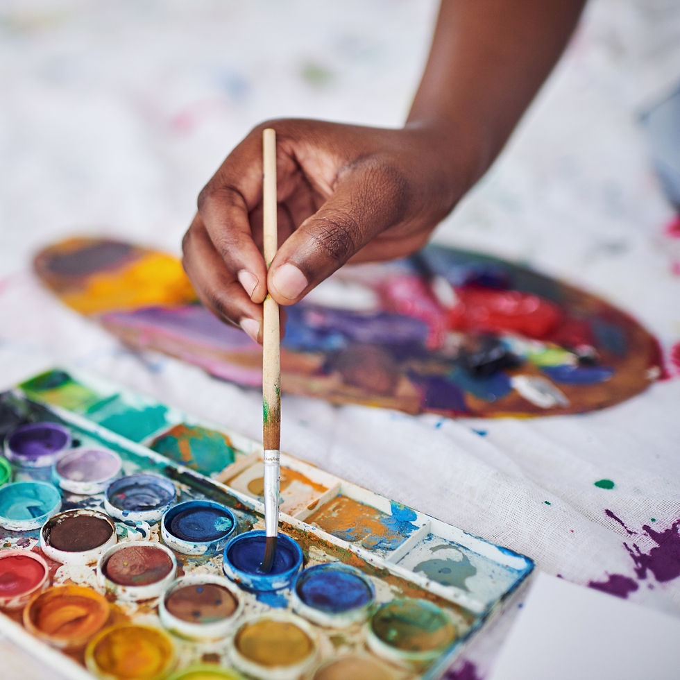adult hand holding a paint brush and dipping it into a palette of watercolour paints.