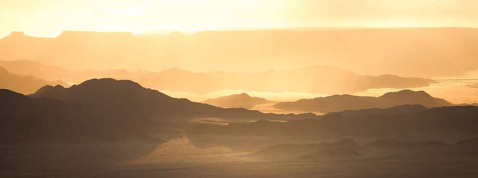 Dramatic view of sunset over the Naukluft Mountains and Namib Desert, the flat-topped mountains glowing orange and yellow, by Will Gray Photography
