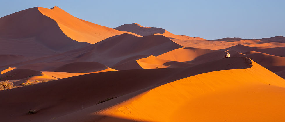 Two people surrounded by the huge sand dunes of the Namib Desert at Sossusvlei in Namibia, photographed by Will Gray in the early morning