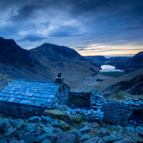 Stone cottage ruins overlooking a valley lake at dusk