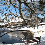 Snowy Cotswolds village pond with a stone house